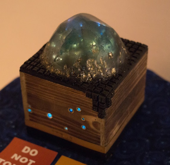 Third Place, Fine Art Category, a crystal-like sculpture glows atop a box