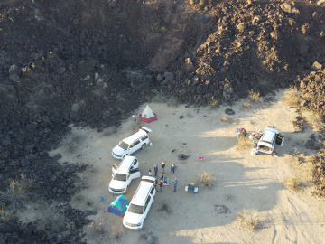 Vans, tents, and field trippers setting up at the base of a volcanic rock pile. Drone image by Nathan Hadland