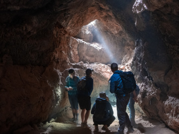 Field trip participants stand in a light beam coming from the entrance to the lava tunnel the group hiked in. Image by Harry Tang