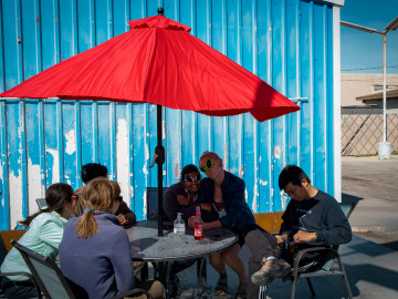 Students take a break at a colorful picnic table in front of a shipping container. Two students are wearing goofy alien sunglasses. Image by Harry Tang.