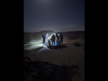 Students observe nature in the desert with headlamps at night pointing off in different directions. Image by Robert Melikyan