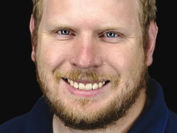 Blond person smiling at camera against a dark background