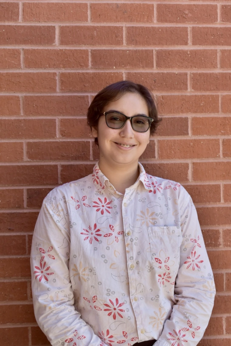 Person with short brown hair smiling at camera, standing in front of a red brick wall