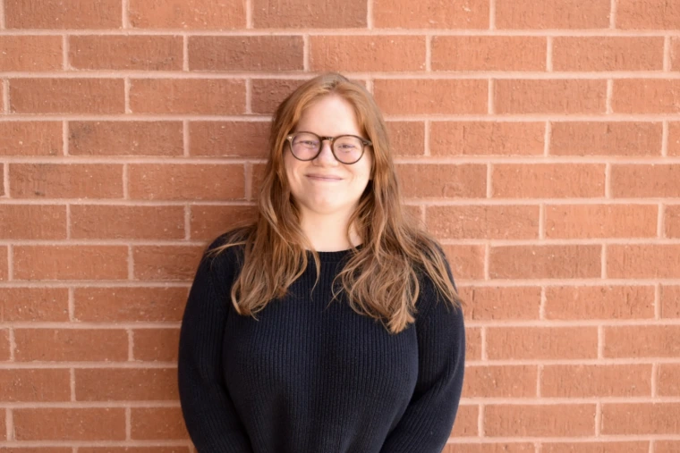 person smiling at camera against brick wall