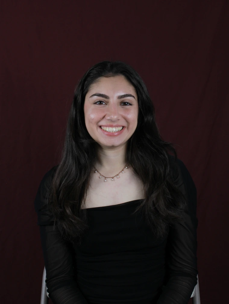 Student smiling at camera with long dark hair against a dark background