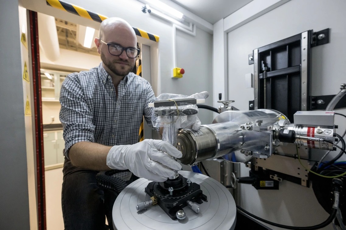 Scott Eckley demonstrates placing a container holding a piece of asteroid material in an X-ray Computed Tomography machine
